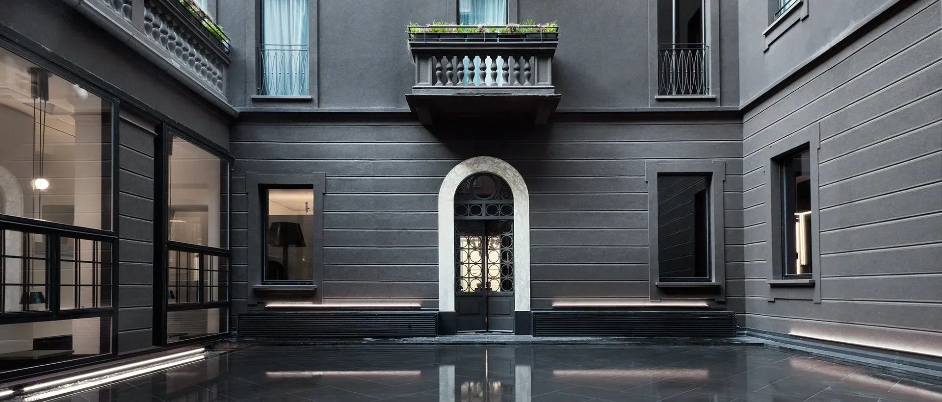The still, dark inner courtyard of the hotel, with a pool of water reflecting the grey palazzo facade and an arched doorway.